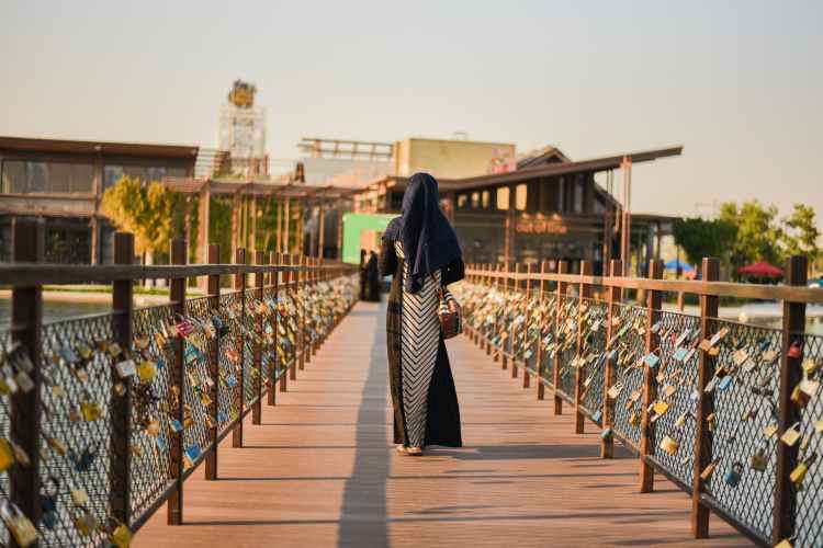 person walking on wooden pathway beside different padlocks hanging on gray stainless steel chain link fence