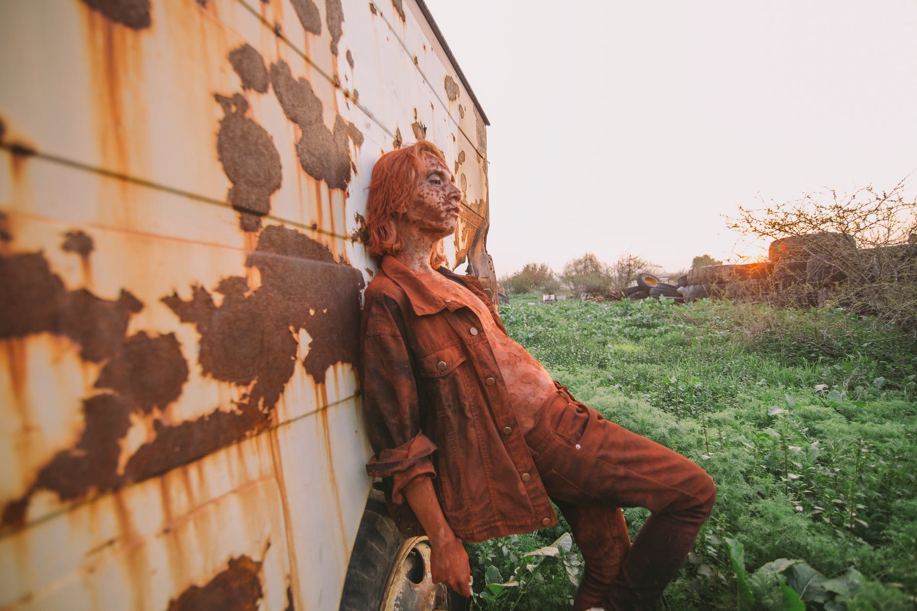 man wearing brown button up jacket and pants leaning on wall