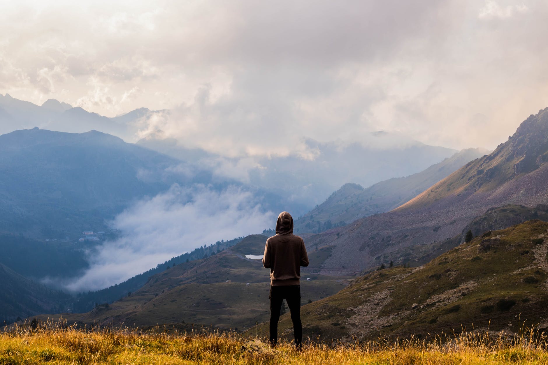 person wearing brown pullover and black jeans standing on mountain top with the scenic view