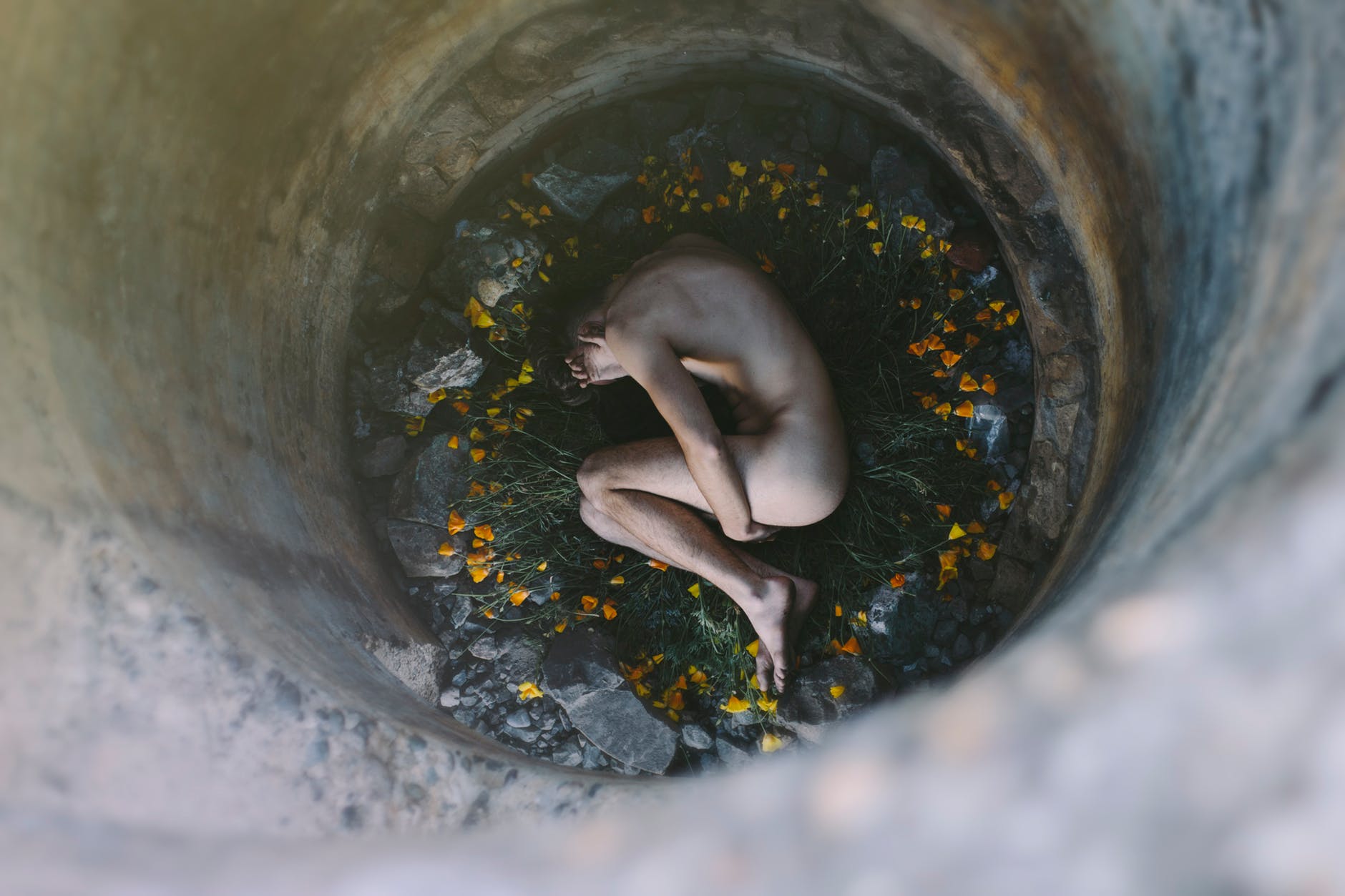 nude person inside well laying on flowers