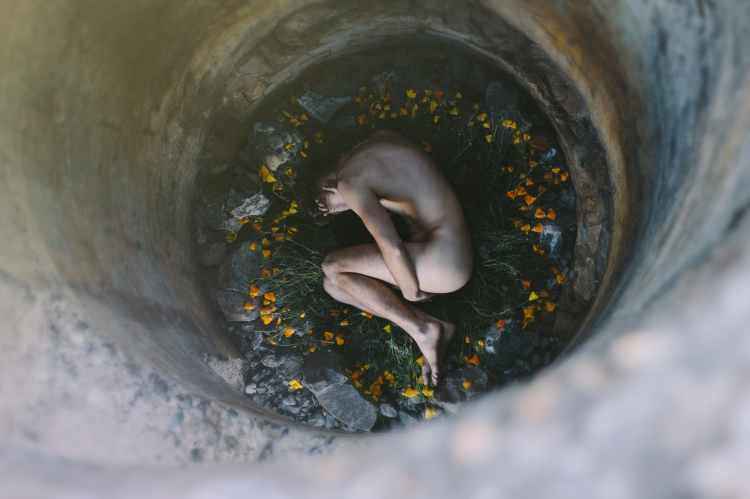 nude person inside well laying on flowers